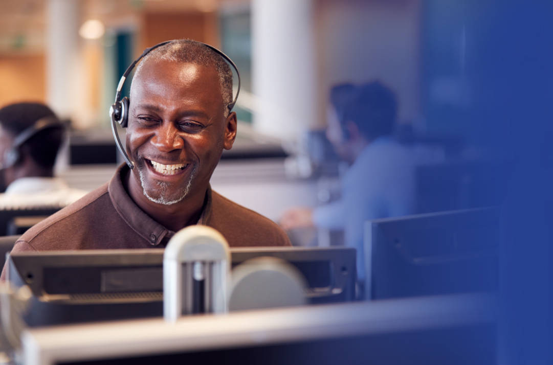 Customer service man with headset and big happy smile in front of a computer monitor