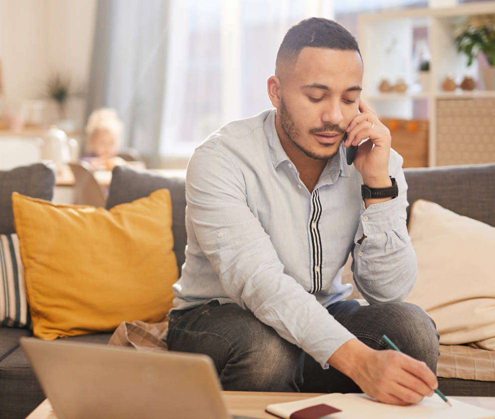 Man working from home, on the phone and taking notes with child in background