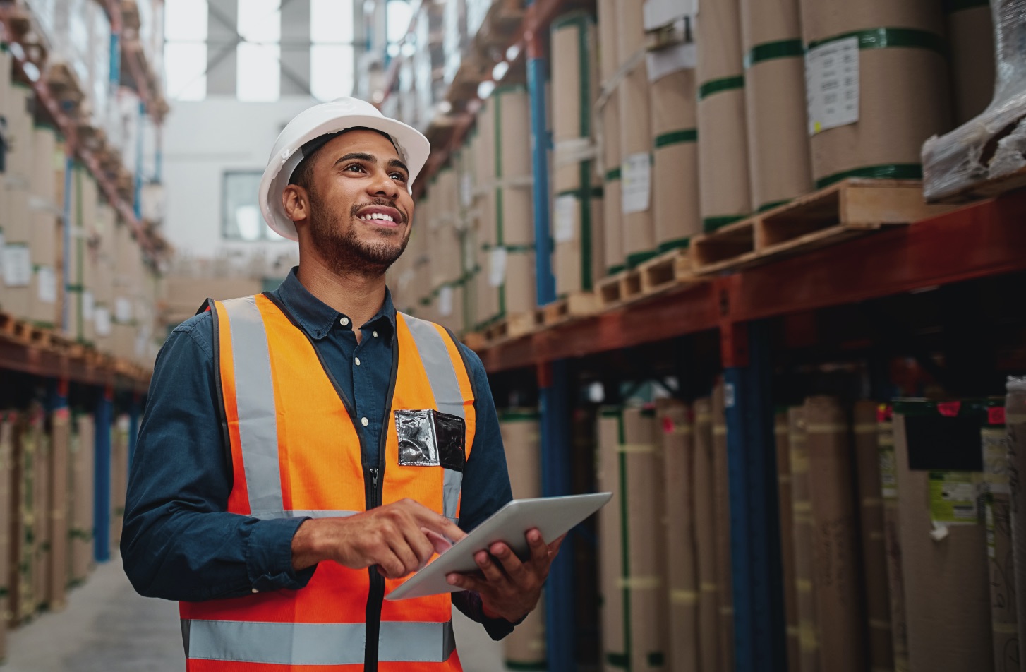 Man with hardhat and reflective vest looking up with a tablet in hand