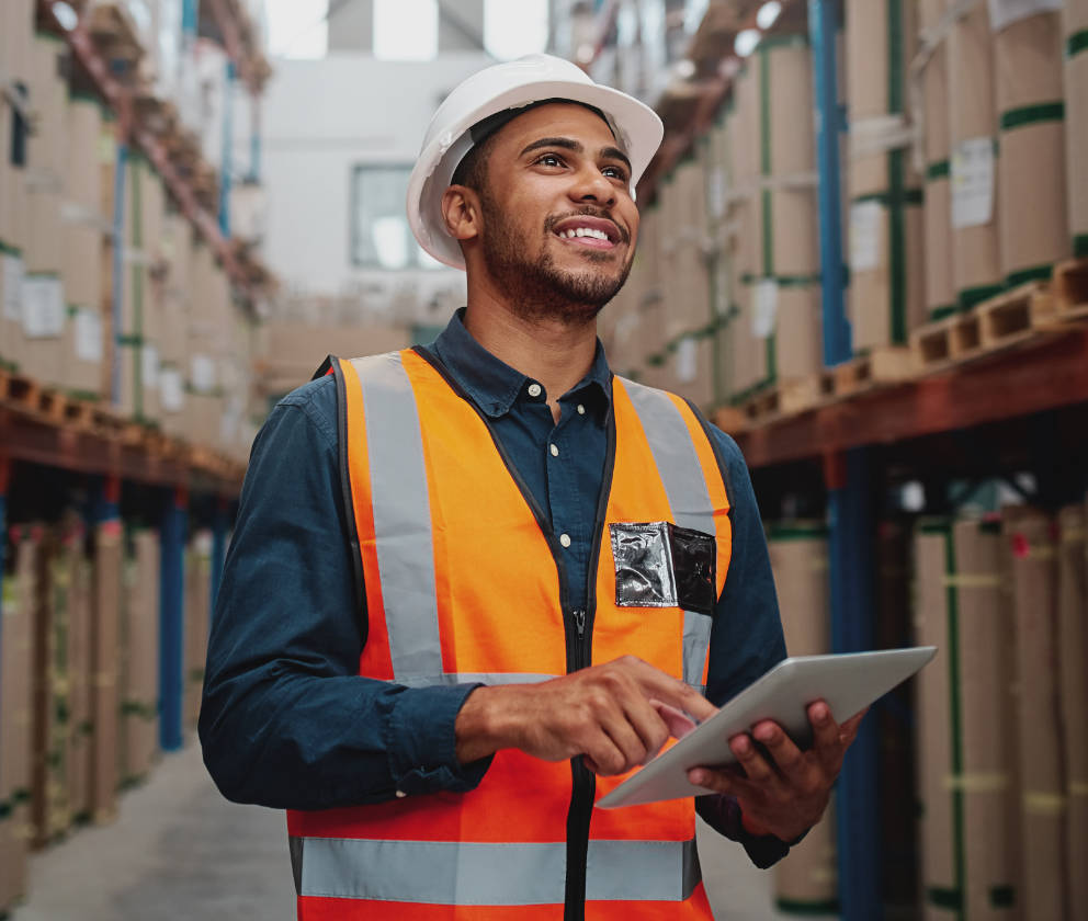 Man with hardhat and reflective vest looking up with a tablet in hand