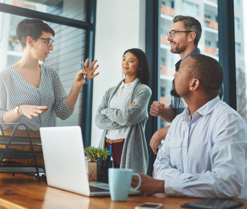 Woman colleague presenting to another woman and three men by a table