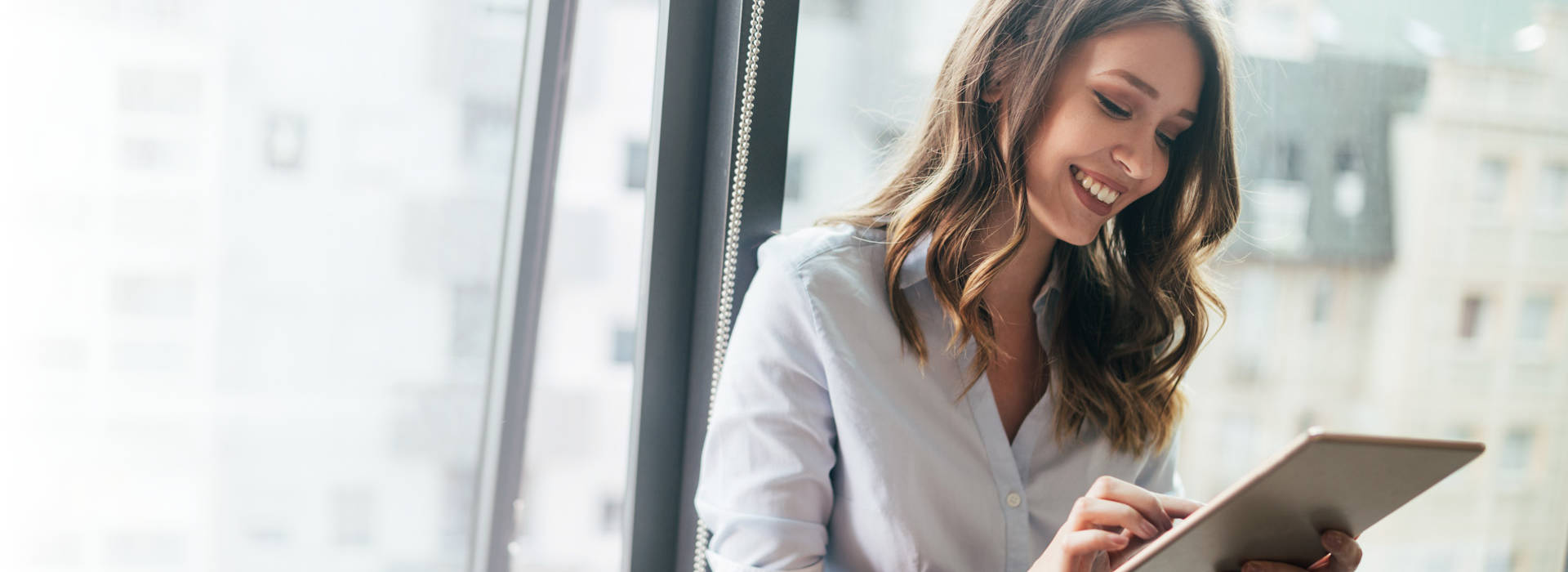 Young businesswoman using a digital tablet while standing in front of windows in office