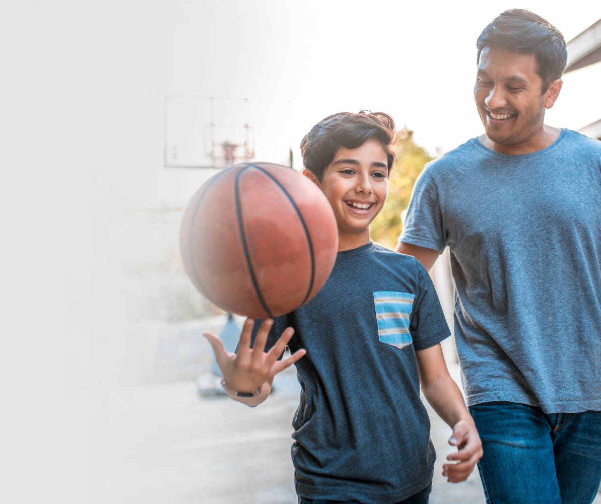 Dad smiling and patting son on back, with son smiling and spinning a basketball