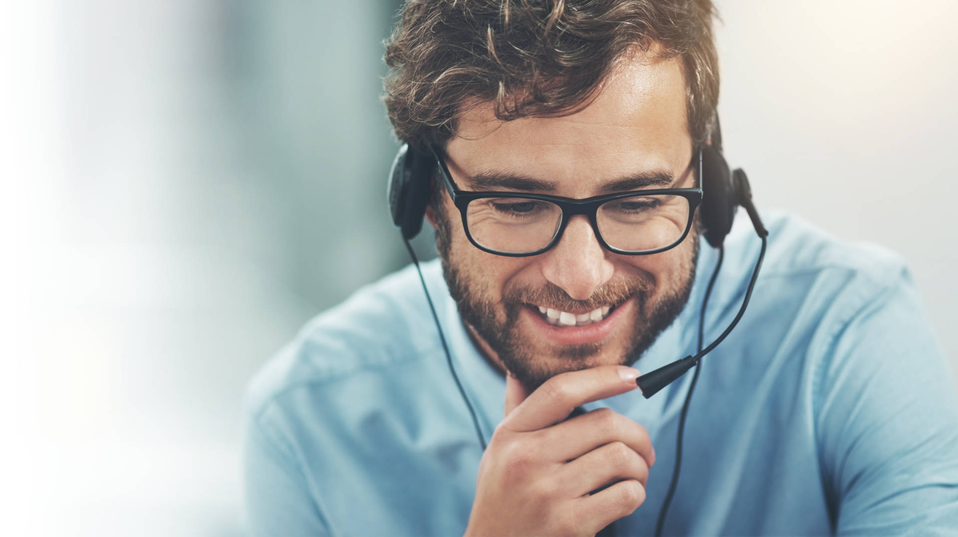 Customer service man with glasses and headset leaning forward with chin in hands and smiling