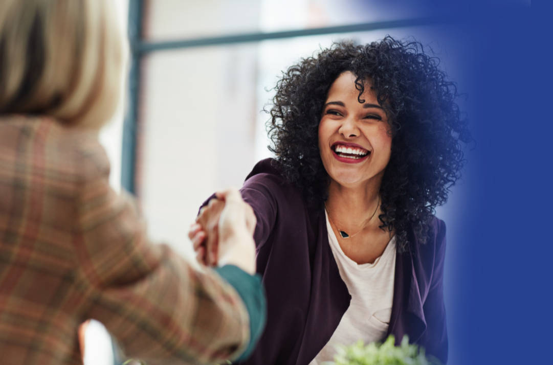 Woman with big happy smile reaching across a table and shaking hands with another woman