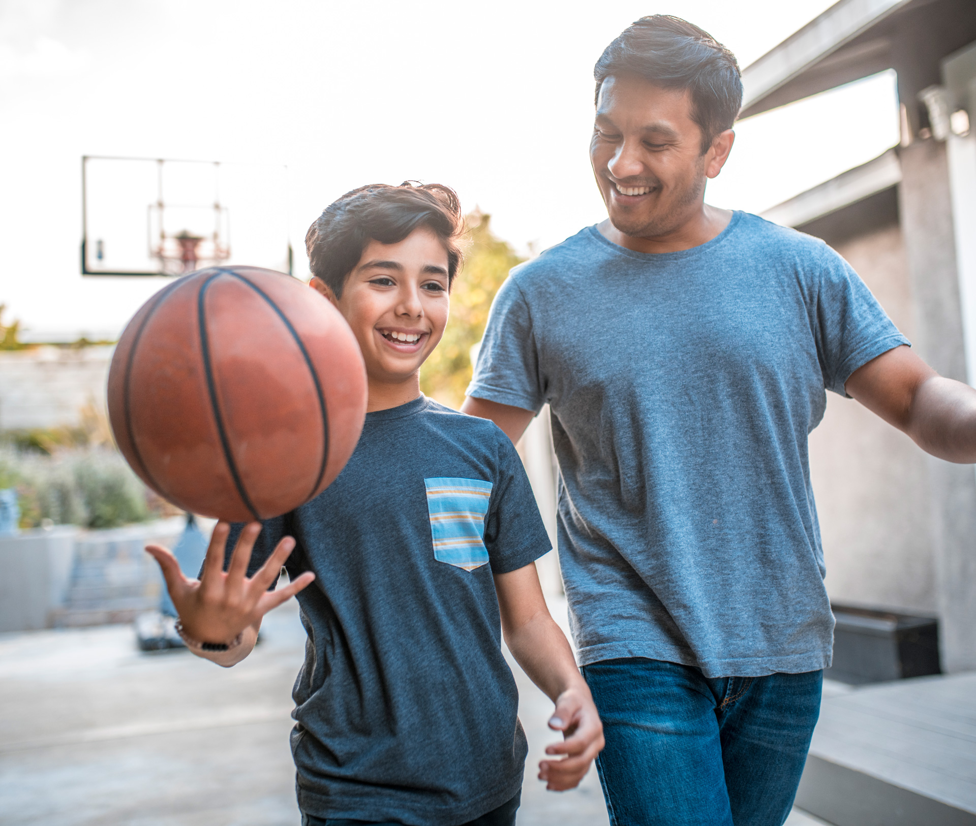 Dad smiling and patting son on back, with son smiling and spinning a basketball