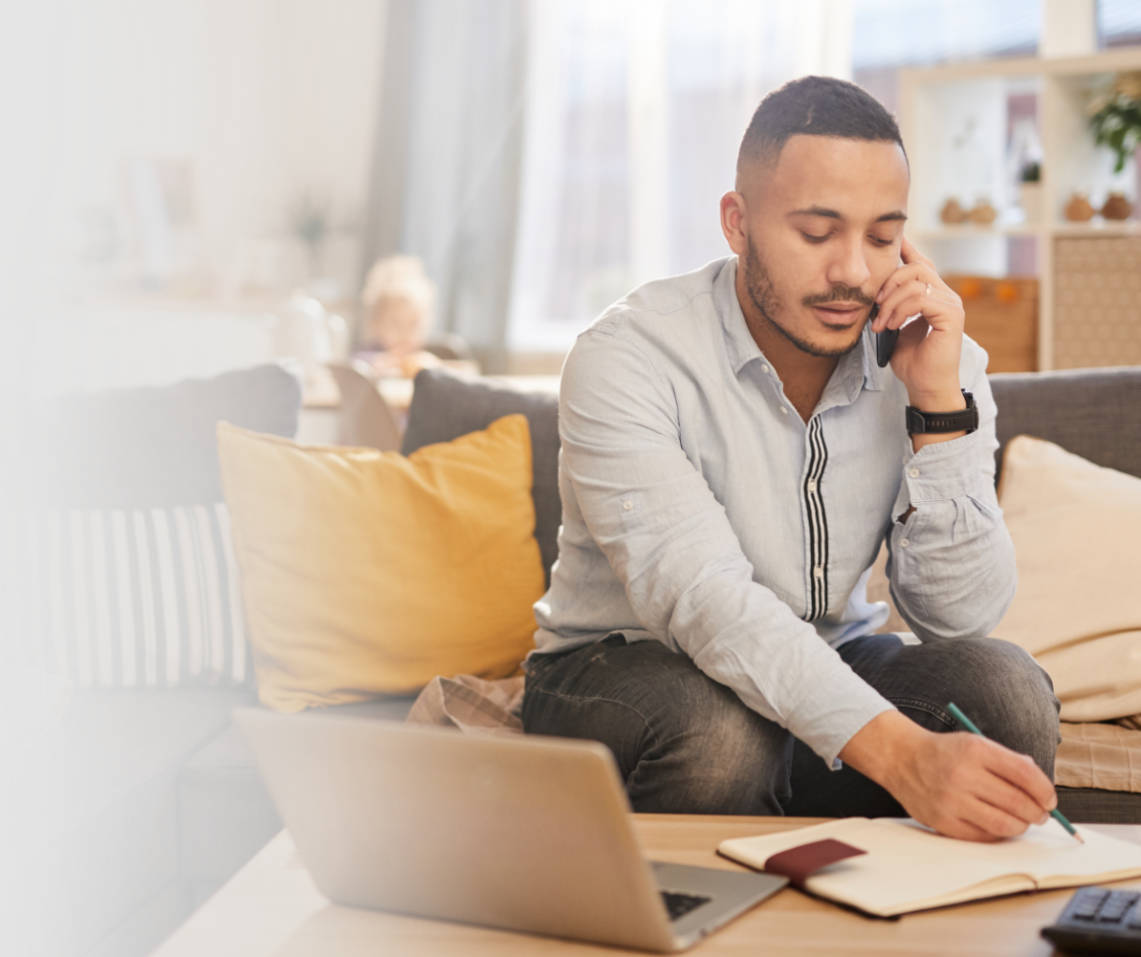 Man working from home, on the phone and taking notes with child in background