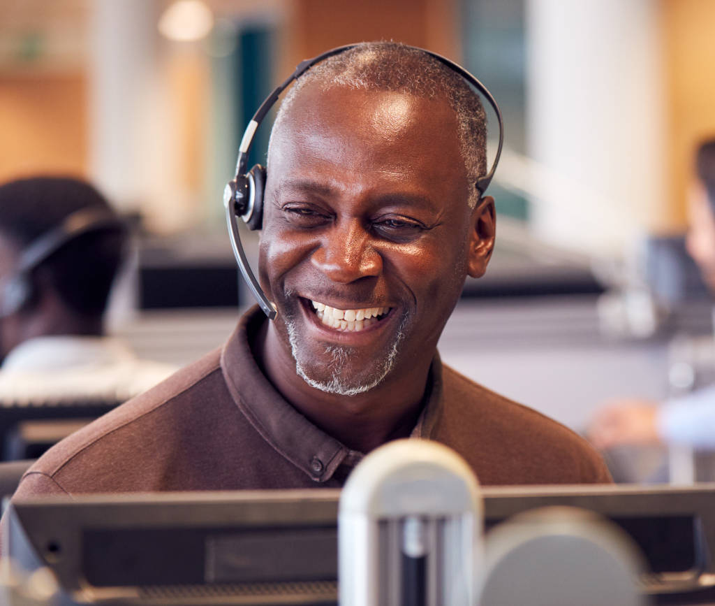 Customer service man with headset and big happy smile in front of a computer monitor