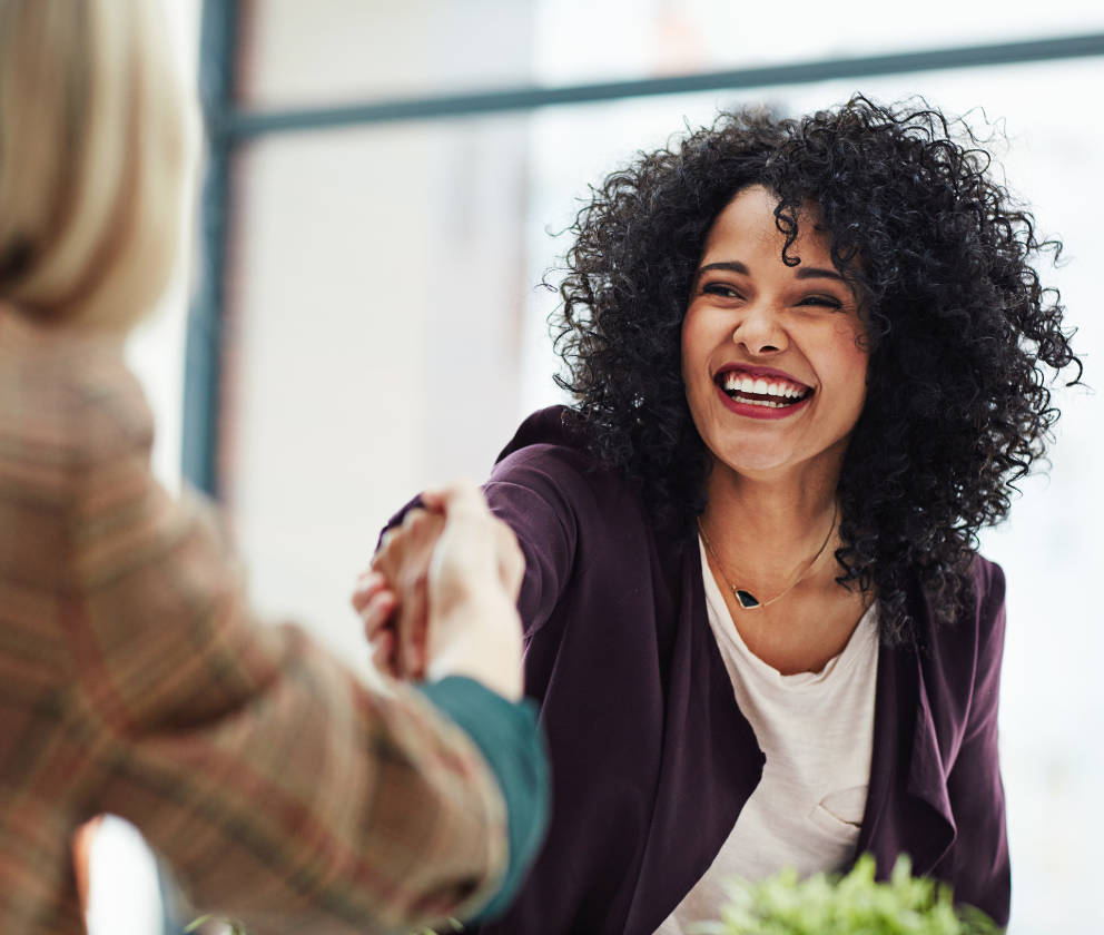 Woman with big happy smile reaching across a table and shaking hands with another woman