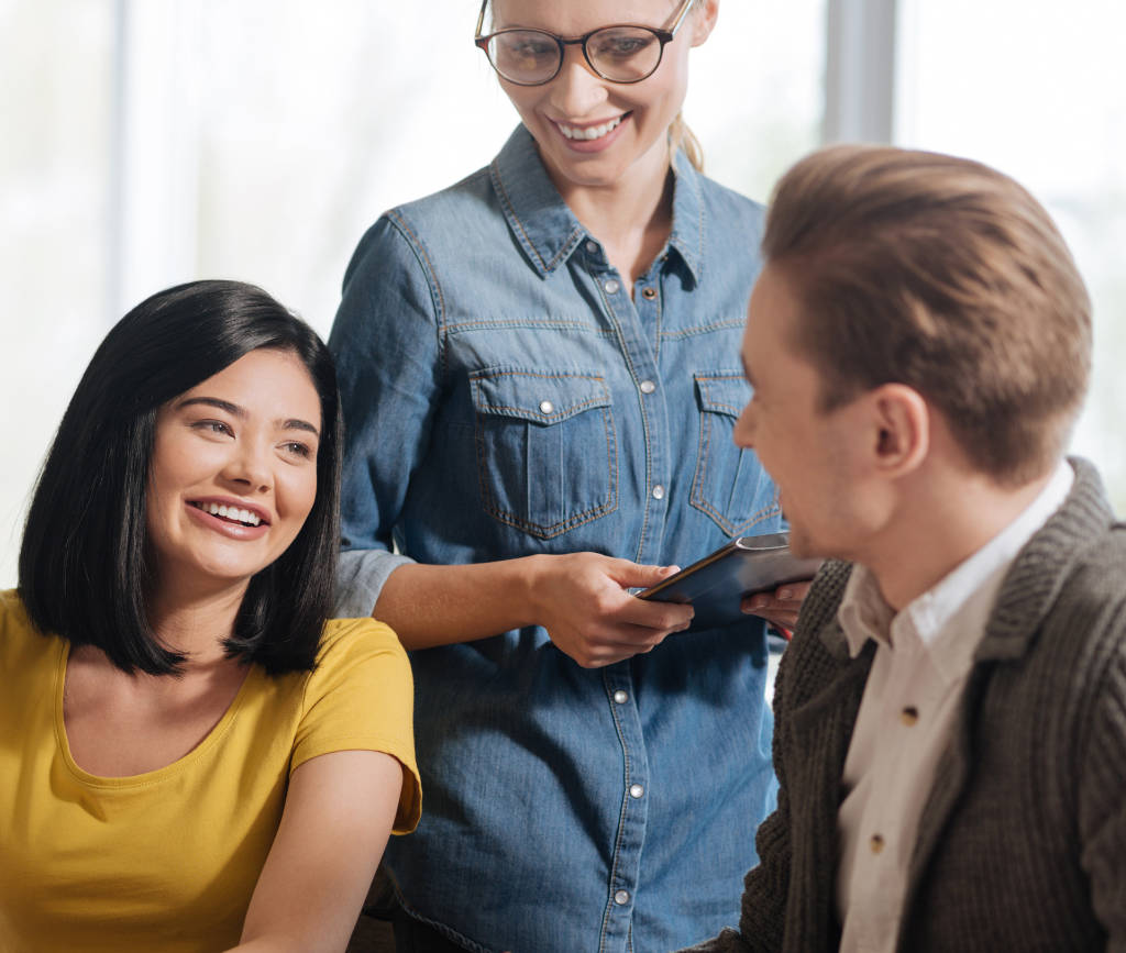 Three colleagues by a table with plans laid out and holding a set square, tablet and pencil