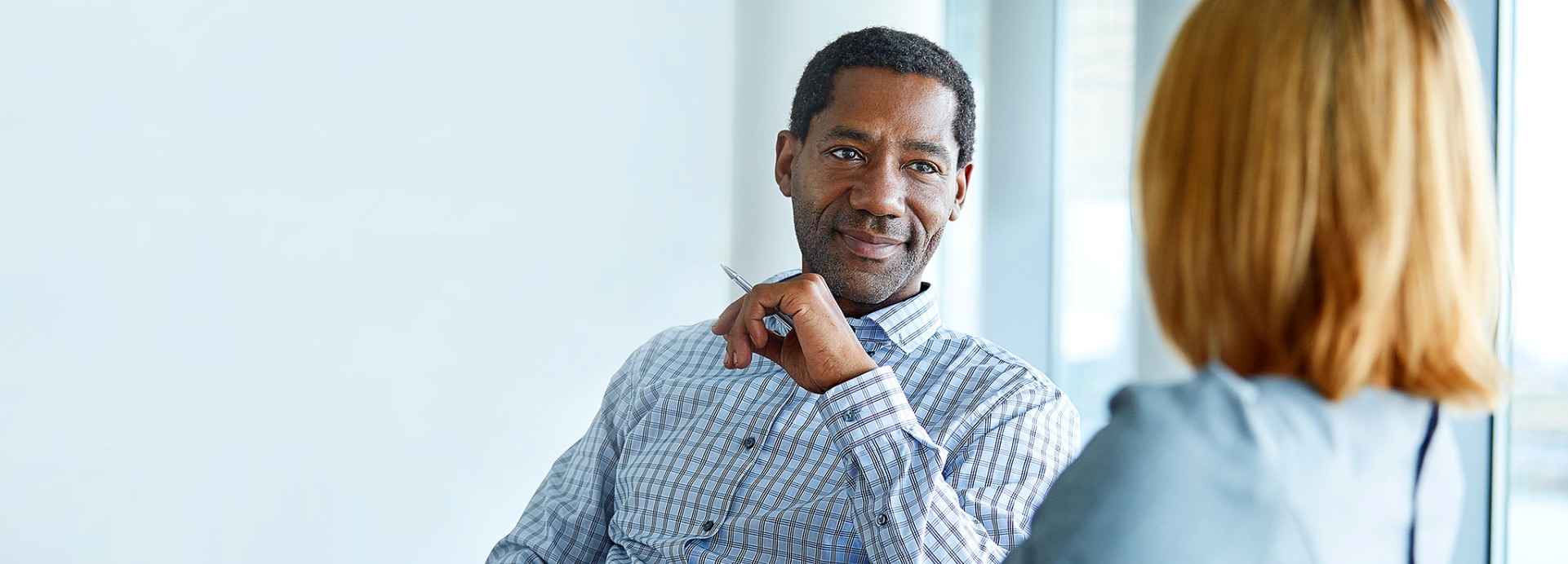 Man leaning back in chair with pen in hand,attentively listening to woman across table