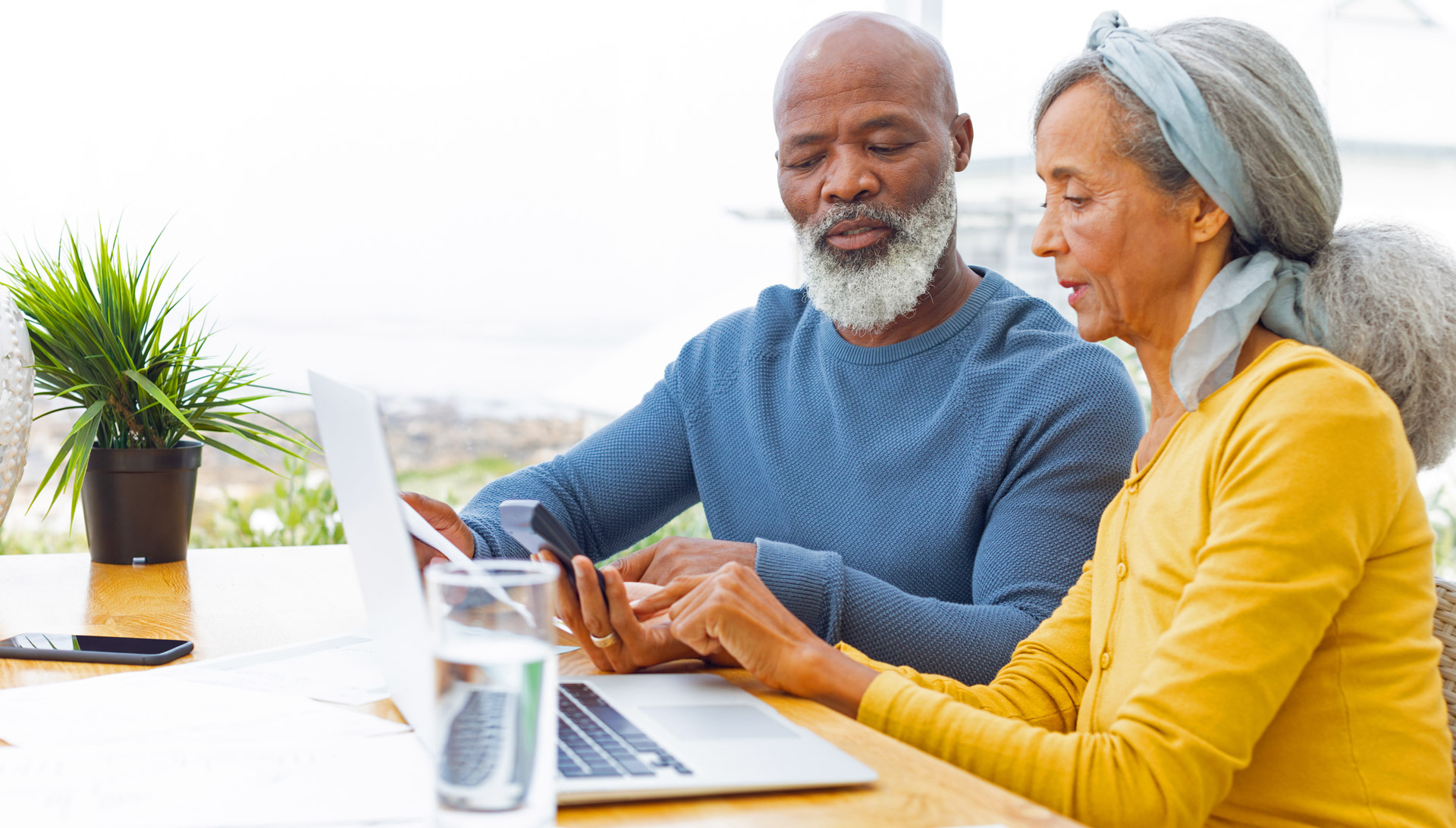 A man and a woman looking up information on a computer while holding a calculator.