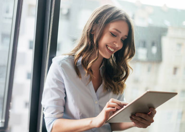 Young businesswoman using a digital tablet while standing in front of windows in office