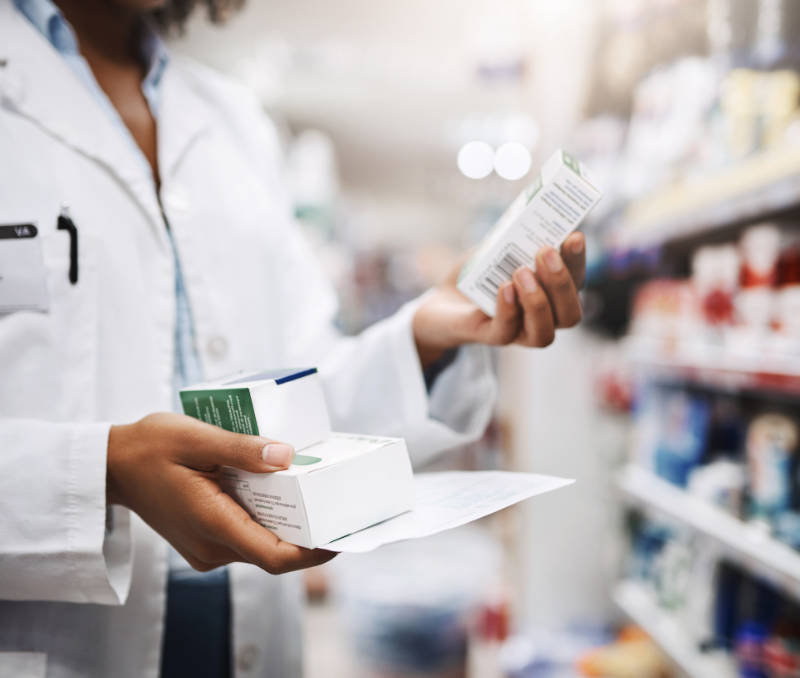 Pharmacist holding a paper and two medicine boxes in one hand and one medicine box in other