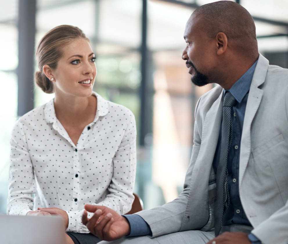 A man and woman coworker sitting down and engaging in conversation