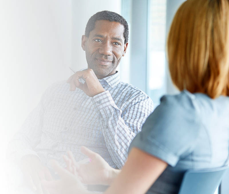 Man leaning back in chair with pen in hand,attentively listening to woman across table